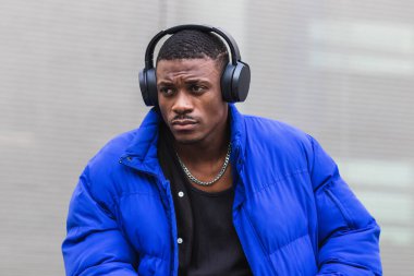 Sakin etnik erkek, şık hippi kıyafetleri içinde, taştan bir sınırda, kulaklıklarla oturuyor ve başka tarafa bakarken şarkılardan keyif alıyor.