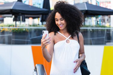 Afrika kökenli Amerikalı bir kadın bebek bekliyor. Merdivenlerde duruyor ve cep telefonlarını karıştırıyor.