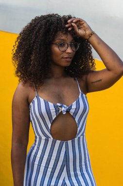 Şık çizgili elbiseli, gözlüklü, kıvırcık saçlara dokunan genç siyahi bir kadın şehrin sokağında canlı bir duvarın yanında duruyordu.