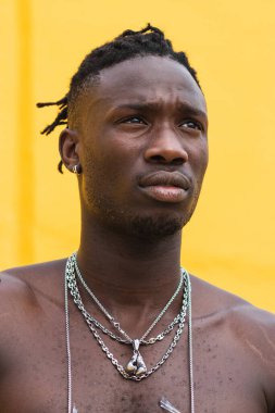 Sarı arka planda çıplak gövdeli, metal zincirli, ciddi Afrikalı genç bir Amerikalı.