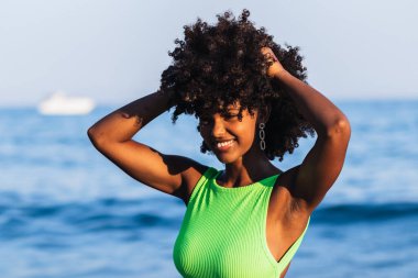 Mayo giymiş, kıvırcık saçlı ve yaz tatilinde eğlenen neşeli Afro-Amerikan kadın.