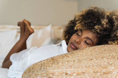 Çekici, kıvırcık saçlı, evde dinlenirken gözleri kapalı yatan Afro-Amerikan kadın.