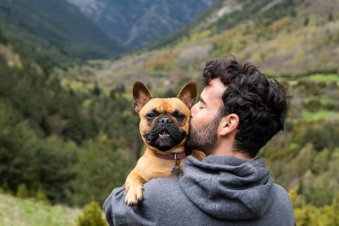 Pireneler 'deki dağ sırasındaki macera sırasında kaya üzerinde oturup Fransız Bulldog' u öpen içerikli erkek yürüyüşçünün arka planı
