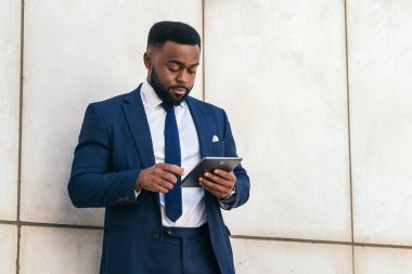 Dışarıda tablet kullanan takım elbiseli bir siyahi işadamının alçak açısı. Yoğunlaşmış görünüyor.