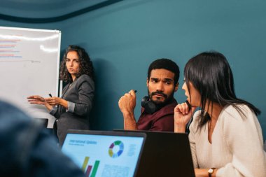 İş kadını, modern bir çalışma alanında iş arkadaşlarıyla birlikte şirket verilerini analiz eden bir toplantıya liderlik ediyor.
