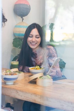 Camdan neşe saçan kadın, yemek yiyen, hafta sonunu beraber geçirirken akıllı telefon kullanan ekinlerle aynı masada oturuyor.