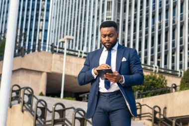 Dışarıda tablet kullanan takım elbiseli bir siyahi işadamının alçak açısı. Yoğunlaşmış görünüyor.