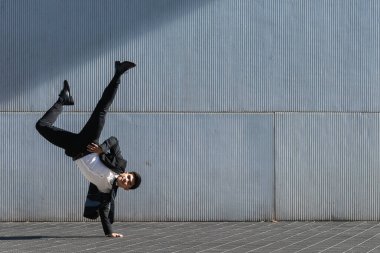 Resmi takım elbiseli Asyalı bir girişimci Breakdance hareketini ve şehir caddesinde kameraya bakarken amuda kalkarken dengeyi sağlıyor.