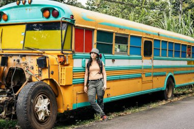 Doğada klasik sarı bir otobüse yaslanan maceraperest bir kadın. Otobüs tazminat alıyor.