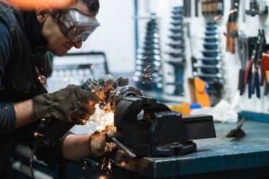 Garajda çalışırken metal işleme aletleriyle metal kesen günlük giysiler, koruyucu gözlükler ve eldivenler giyen yetişkin erkek tamircinin yan görüntüsü.