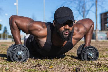 Spor giyimli genç, kaslı siyah erkek sporcunun zemin seviyesi. Şehirde halterlerle egzersiz yapıyor.