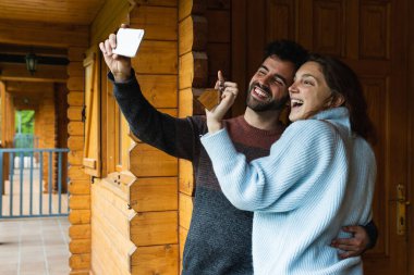 Yeni ahşap kulübenin anahtarlarıyla neşeli bir çift. Pireneler 'de kucaklaşıp cep telefonundan kendilerini vuruyorlar.