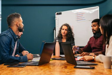 İş kadını, modern bir çalışma alanında iş arkadaşlarıyla birlikte şirket verilerini analiz eden bir toplantıya liderlik ediyor.