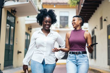 Siyahi kadınlar şık arkadaşlarıyla sokakta yürürken akıllı telefon kullanarak eğleniyorlar.