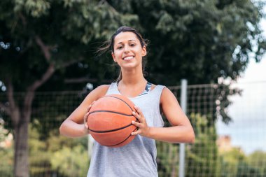 Bir bayan basketbolcunun portresi, kendine güvenen bir basketbol topu tutuyor.