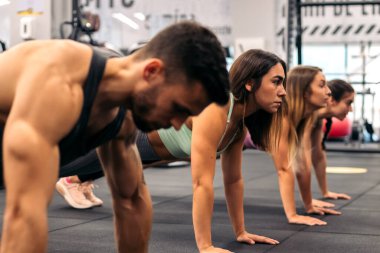 Spor salonunda şınav çeken bir grup genç.