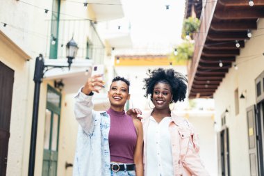 Tarz sahibi siyahi kadın arkadaşlar sokakta yürürken eğleniyor ve gülüyorlar.