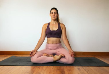 Pembe spor kıyafetli genç bir kadın evde yoga yapıyor. Lotus Pozu.