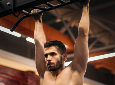 Erkek sporcu spor salonunda barfiks çekiyor.