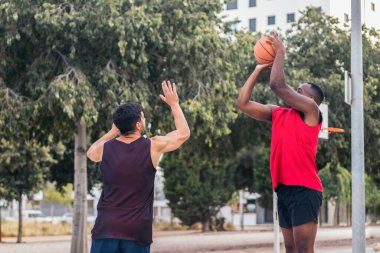 Genç erkek sporcular şehirdeki bir sahada spor giyim sektöründe basketbol oynuyorlar.