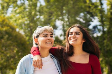 Parkta yürüyen ve gülümseyen iki genç kız.