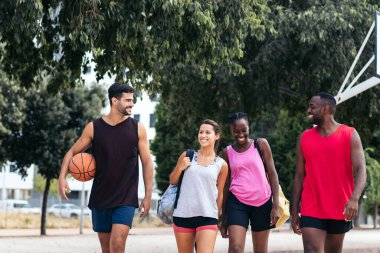 Spor giyimli bir grup ırklar arası arkadaş sahada basketbol oynamaya gidiyorlar.