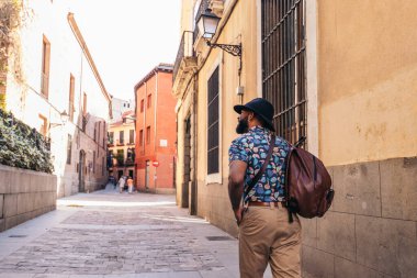 Alternatif hippi görünümlü şık siyah adam güneşli bir yaz gününde şehrin sokaklarında yürüyor.