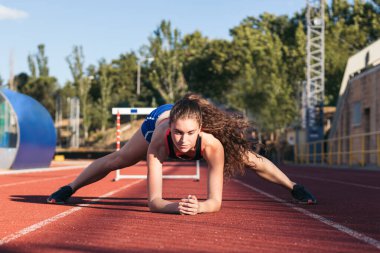 Sportif bir kadın koşmadan önce spor pistinde ısınıyor ve esneklik eğitimi alıyor..