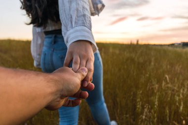 Güzel bir gün batımı olan bir tarlada el ele tutuşan çift.