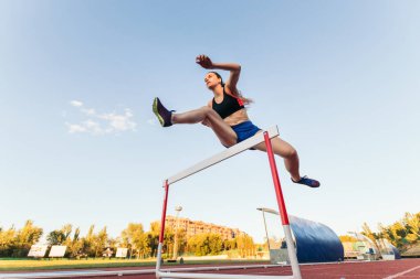 Engelli bir yarış için spor kıyafeti giymiş güçlü bir kadın. Bir atletizm pistinde engellerden atlıyor..
