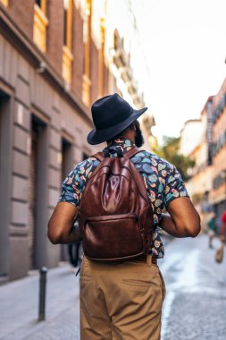 Alternatif hippi görünümlü şık siyah adam güneşli bir yaz gününde şehrin sokaklarında yürüyor..