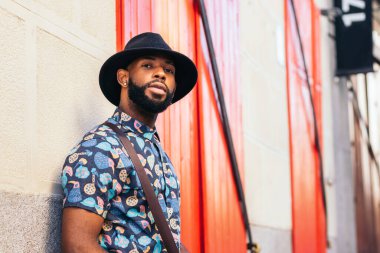 Şehir sokaklarında duvara yaslanan şapkalı ve alternatif kıyafetli şık bir siyahın portresi.