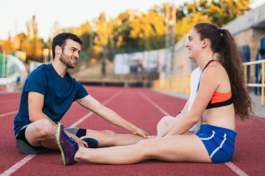 Atletizm antrenmanından sonra yerde oturup esneme hareketleri yapan iki sporcu..