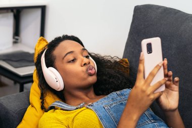 Genç siyahi kadın kanepede uzanıyor, müzik dinliyor ve rahatlamak için kulaklık takıyor.