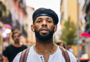 Şehir caddesinde durmuş gülümseyen kameraya bakan bereli ve dövmeli şık bir zenci portresi.