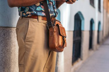 Alternatif kıyafetli şık siyah adam şehrin sokaklarında duvara dayanan akıllı telefon kullanıyor.