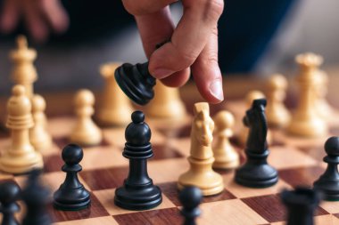 Satranç oynayan bir adamın tanınmaz eli. Rakibinin beyaz şövalyesini yemek için siyah taşlardan birini alır.