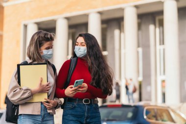 Cep telefonuna bakan maskeli iki öğrenci kız..