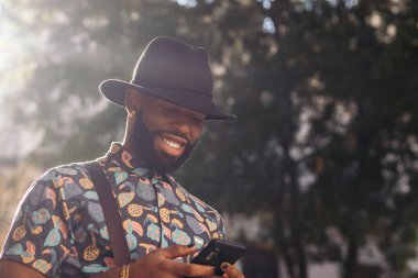 Yazın şehir caddesinde akıllı telefon kullanan şık, şapkalı bir zenci.