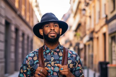 Alternatif hippi görünümlü şık siyah adam güneşli bir yaz gününde şehrin sokaklarında yürüyor..