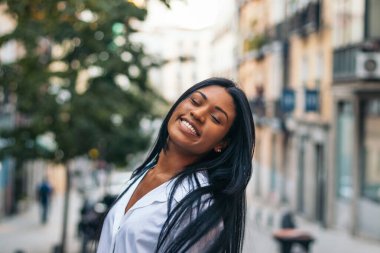 Gözleri kapalı, gülümseyen güzel bir Latin Amerikalı kadının portresi. O, sokakta duruyor ve uzun siyah saçlarının geri çekilmesine izin veriyor. Mutluluk ve iyimserliği iletir..