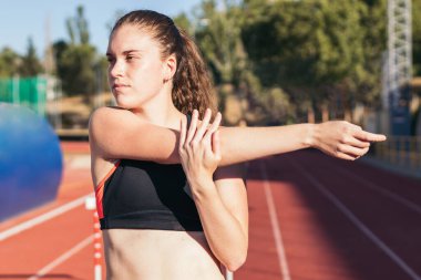 Spor kıyafetli güçlü bir kadın atletizm pistinde koşmadan önce esniyor..