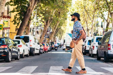 Alternatif hippi görünümlü şık siyah adam güneşli bir yaz gününde şehrin sokaklarında yürüyor. Gülümsüyor.