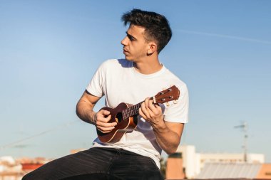 Genç adam bir çatıda ukelele oynuyor.
