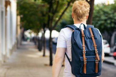 Bir yaz sabahı şehir caddesinde albino yürüyüşü yapan genç bir Latin 'in arka görüntüsü. Beyaz elbiseler ve mavi bir sırt çantası giyiyor..