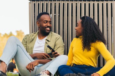 Siyah çift parkta cep telefonuyla oturuyor.