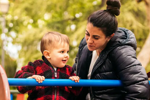 Gülümseyen anne ve bebek oyun bahçesinde oynuyorlar.