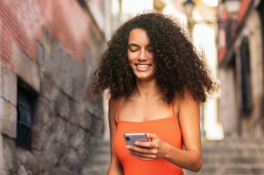 Güzel, kıvırcık saçlı, yürüyen ve cep telefonunu merdivenlerden inerken kullanan genç bir kadın.