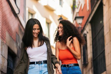 İki genç kadın merdivenlerden aşağı inerken gülümseyerek ellerini tutuyorlar.