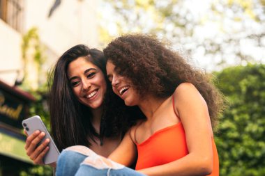 İki güzel kadın cep telefonlarını kullanarak oturuyor.